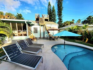 A pool area with lounge chairs, a table with chairs, and a covered umbrella. - Beach House with Ocean View, Heated Pool, and Rooftop Deck! Dog-friendly! (Cocoa Beach)