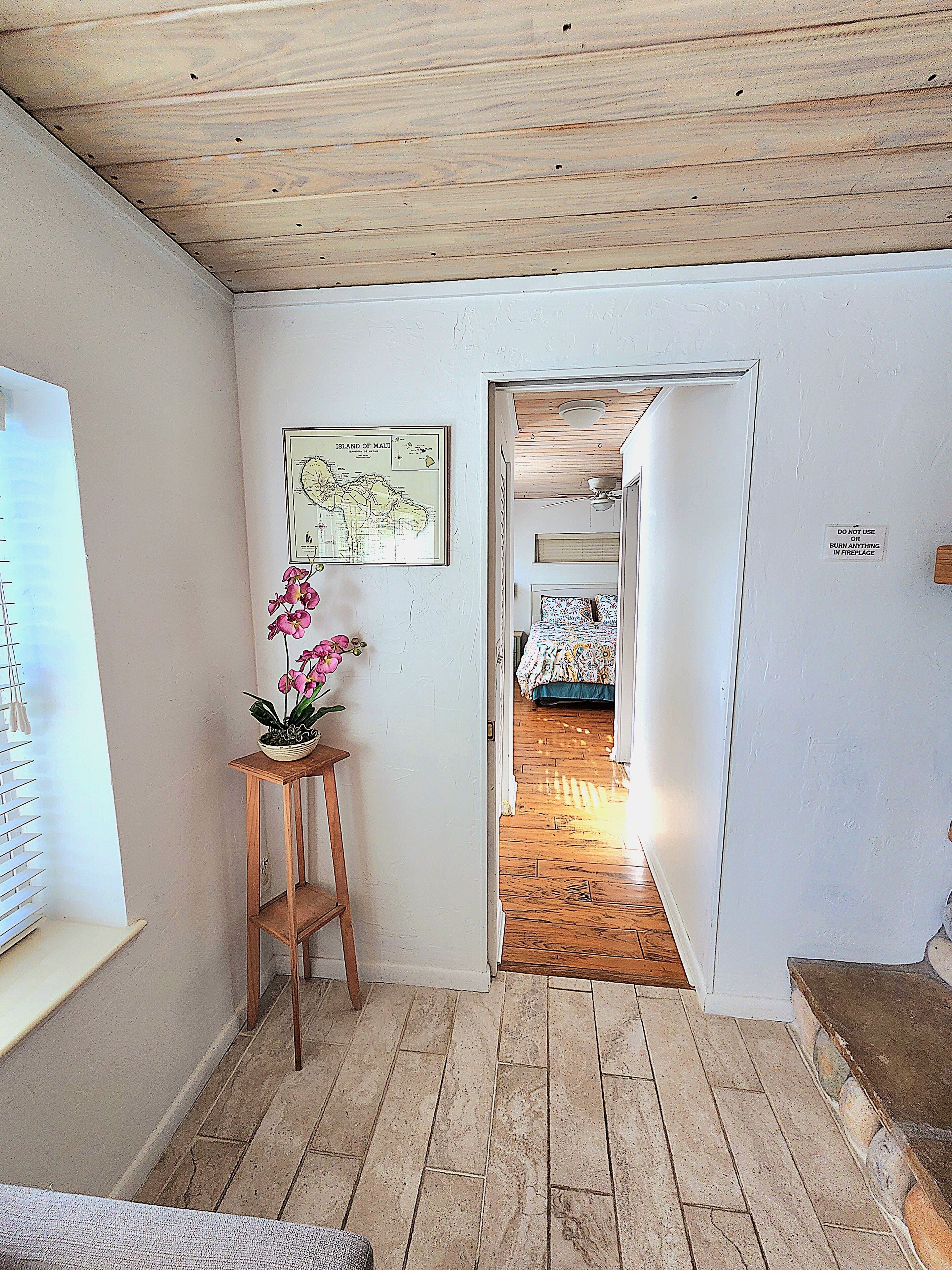 Una habitación con piso de madera, una cama con colcha estampada, un mapa en la pared y un letrero que prohíbe el uso de la chimenea.