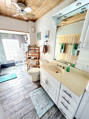 A bathroom with a wooden floor, a beige sink, a white toilet, a towel rack, and a ceiling fan. - Beach House with Ocean View, Heated Pool, and Rooftop Deck! Dog-friendly! (Cocoa Beach)