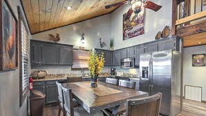 A modern kitchen with dark cabinets, stainless steel appliances, and a wooden dining table with chairs. - Smoky Mountain Loft - UNBELIEVABLE MOUNTAIN VIEWS, Great Location, Free Tickets! (Pigeon Forge)