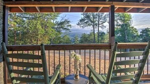 A wooden deck with two green chairs and a small table with a vase. - Smoky Mountain Loft - UNBELIEVABLE MOUNTAIN VIEWS, Great Location, Free Tickets! (Pigeon Forge)