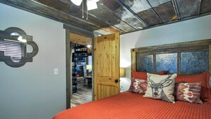 A bedroom with a wooden door, a bed with red bedding, and decorative pillows. - Smoky Mountain Loft - UNBELIEVABLE MOUNTAIN VIEWS, Great Location, Free Tickets! (Pigeon Forge)
