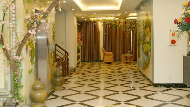 A hotel lobby with a checkered floor, a staircase, a chair, and a wall with a painting. - Nam Son Hotel (Hanoi)