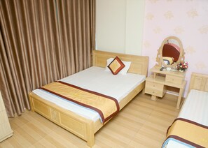 A neatly arranged hotel room with a wooden bed, a bedside table with a mirror, and a dresser. - Nam Son Hotel (Hanoi)