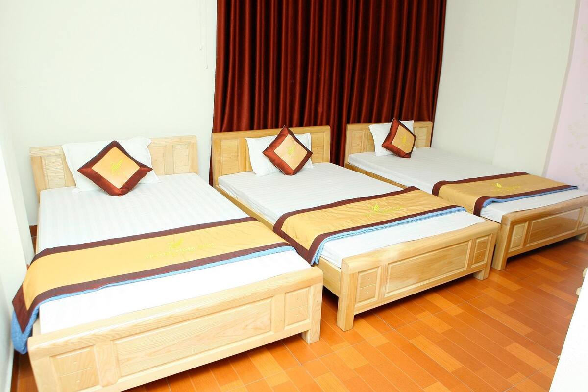 A hotel room with four wooden beds, each with a headboard and footboard, and a brown curtain in the background.