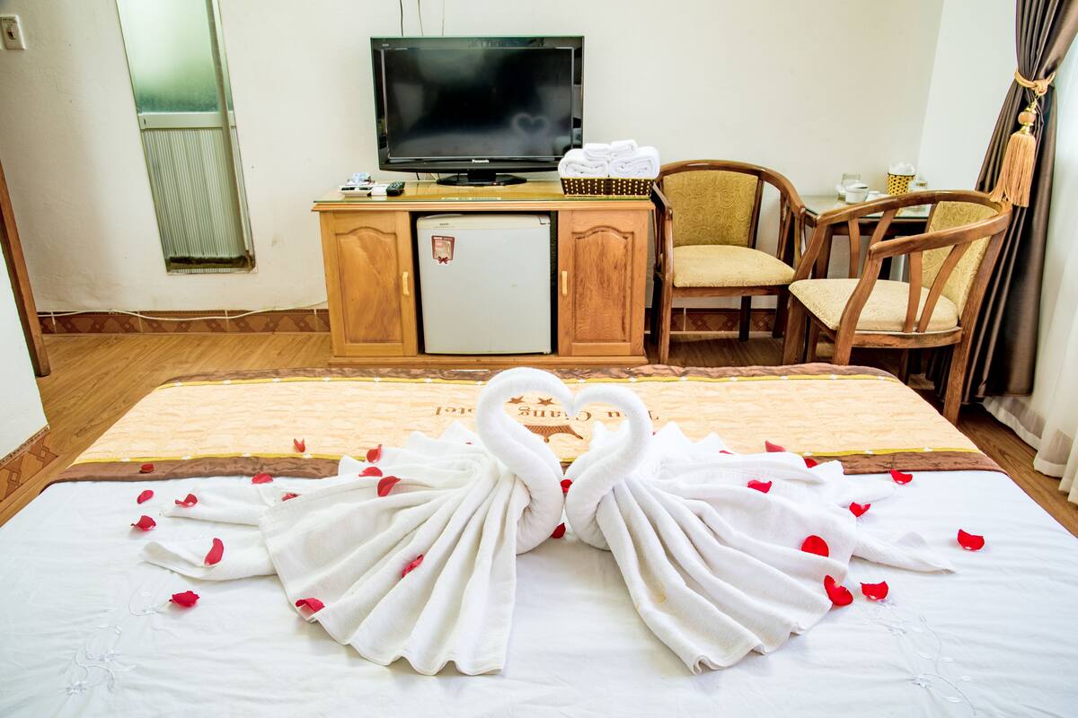A hotel room with a bed, a television, a refrigerator, and two chairs.