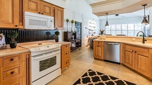 A kitchen with wooden cabinets, a white stove, a microwave, a dishwasher, and a black and white rug. - Marco's Charmer: luxury coastal living, magical sunsets, tranquil water views, relaxing hot tub. (Marco Island)