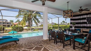 A covered outdoor area with a pool, lounge chairs, a dining table with chairs, and a ceiling fan. - Marco's Charmer: luxury coastal living, magical sunsets, tranquil water views, relaxing hot tub. (Marco Island)