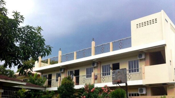 A two-story residential building with balconies, air conditioning units, and a garden area with pink flowering plants. - Spurlock Residences (Lapu-Lapu)