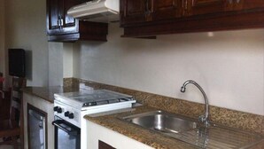 A kitchen with a stove, sink, and wooden cabinets. - Spurlock Residences (Lapu-Lapu)