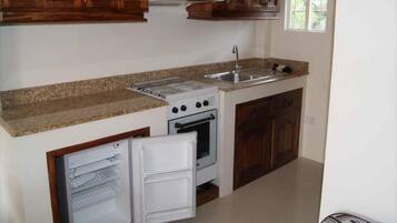 A compact kitchen with wooden cabinets, a built-in oven, a refrigerator, and a granite countertop.