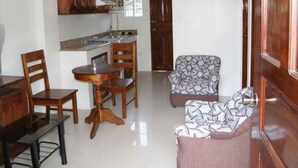 A compact kitchen with wooden cabinets, a dining table with chairs, and a patterned armchair. - Spurlock Residences (Lapu-Lapu)