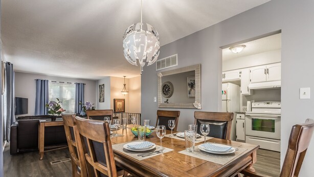 A dining area with a wooden table set for four, surrounded by chairs. There is a chandelier above the table, and a kitchen is visible in the background. - Comfortable and elegant 3BDR duplex, unit # 3 (Overland Park)