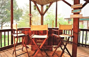 Um deck de madeira com quatro cadeiras dobráveis, uma pérgula de madeira e uma placa que diz 'FLAMINGO Lounge'.