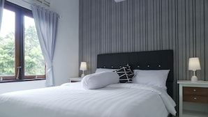 A neatly made bed with white linens, a black headboard, and two bedside tables with lamps. - Sayana Homestay (Sleman)