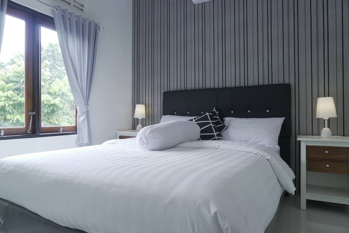 A neatly made bed with white linens, a black headboard, and two bedside tables with lamps.