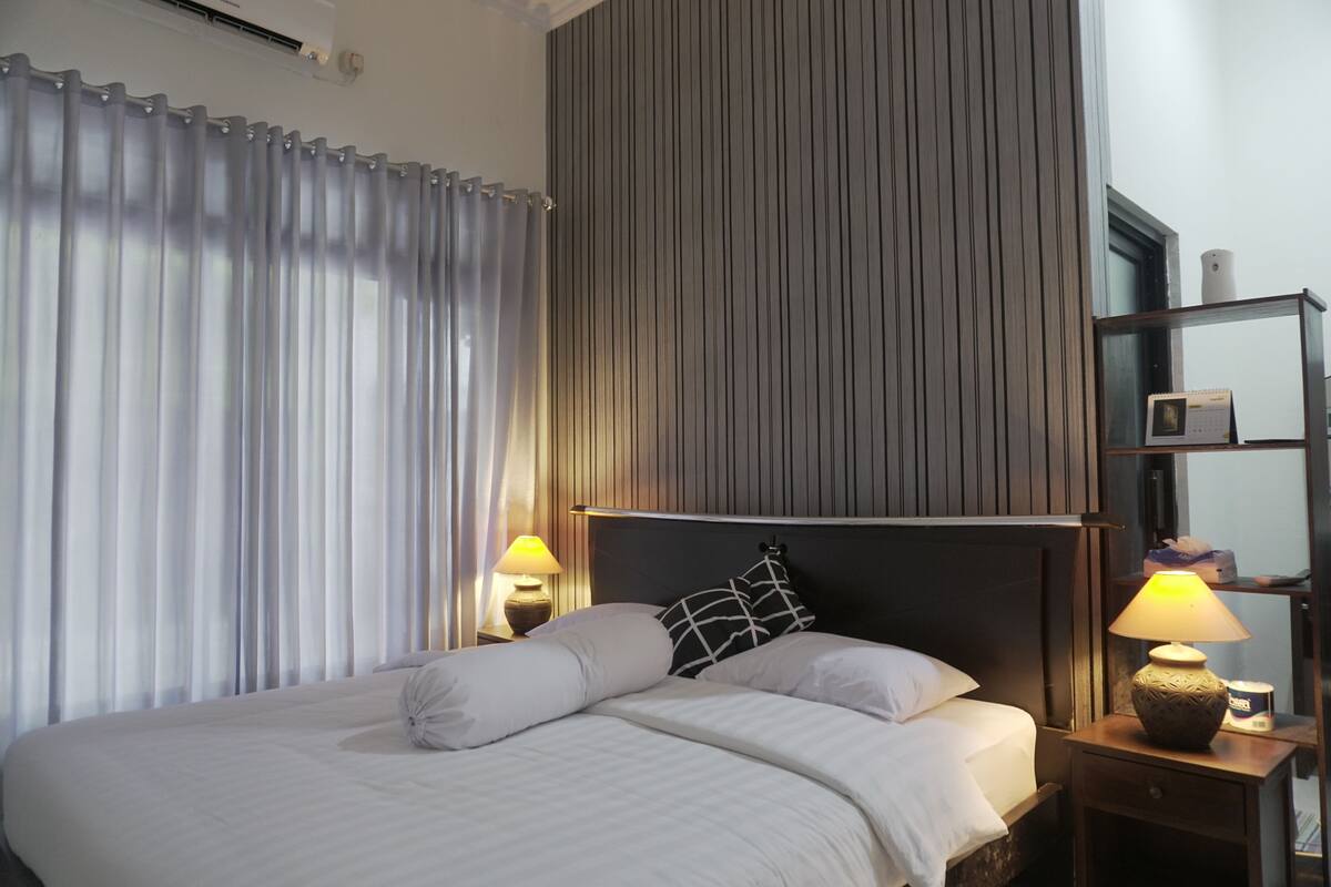 A neatly made bed with white linens and a black and white pillow, a bedside lamp, and a small table with a lamp and a tissue box.