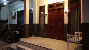 A building entrance with a wooden door, steps, and a bench. - Sayana Homestay (Sleman)