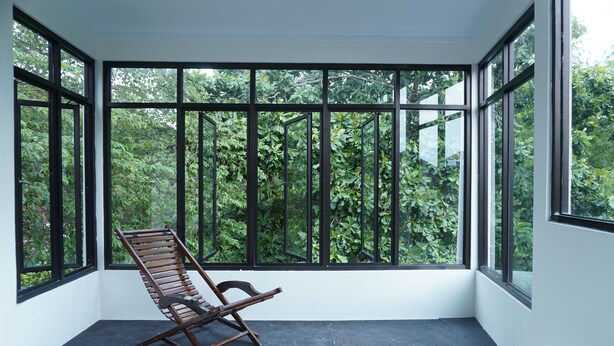 A room with large windows, a wooden chair, and a black mat on the floor. - Sayana Homestay (Sleman)