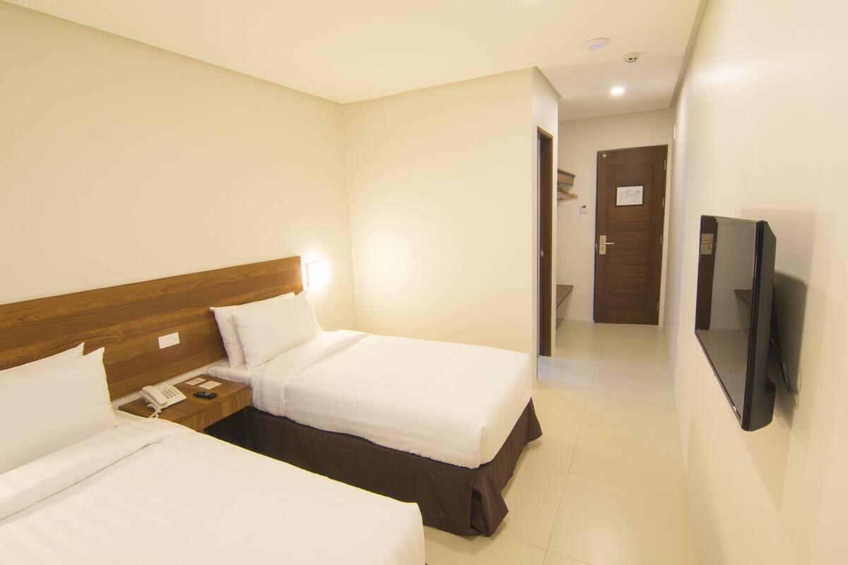 Une chambre d’hôtel avec deux lits, une télévision, un téléphone et une porte donnant sur une salle de bain.