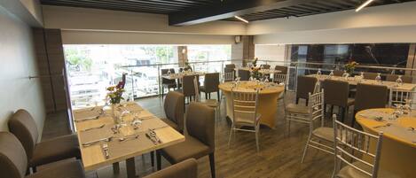 Un restaurante moderno con varias áreas de comedor, incluidas mesas redondas y rectangulares, y una combinación de sillas de metal y tapizadas.
