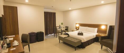 A hotel room with a bed, bedside table, desk, chair, and a small table with a plant.