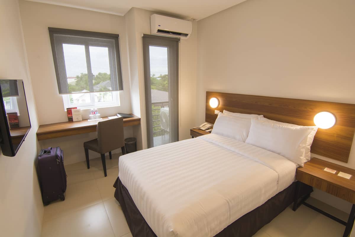 Une chambre d’hôtel avec un lit, un bureau, une chaise et une valise.