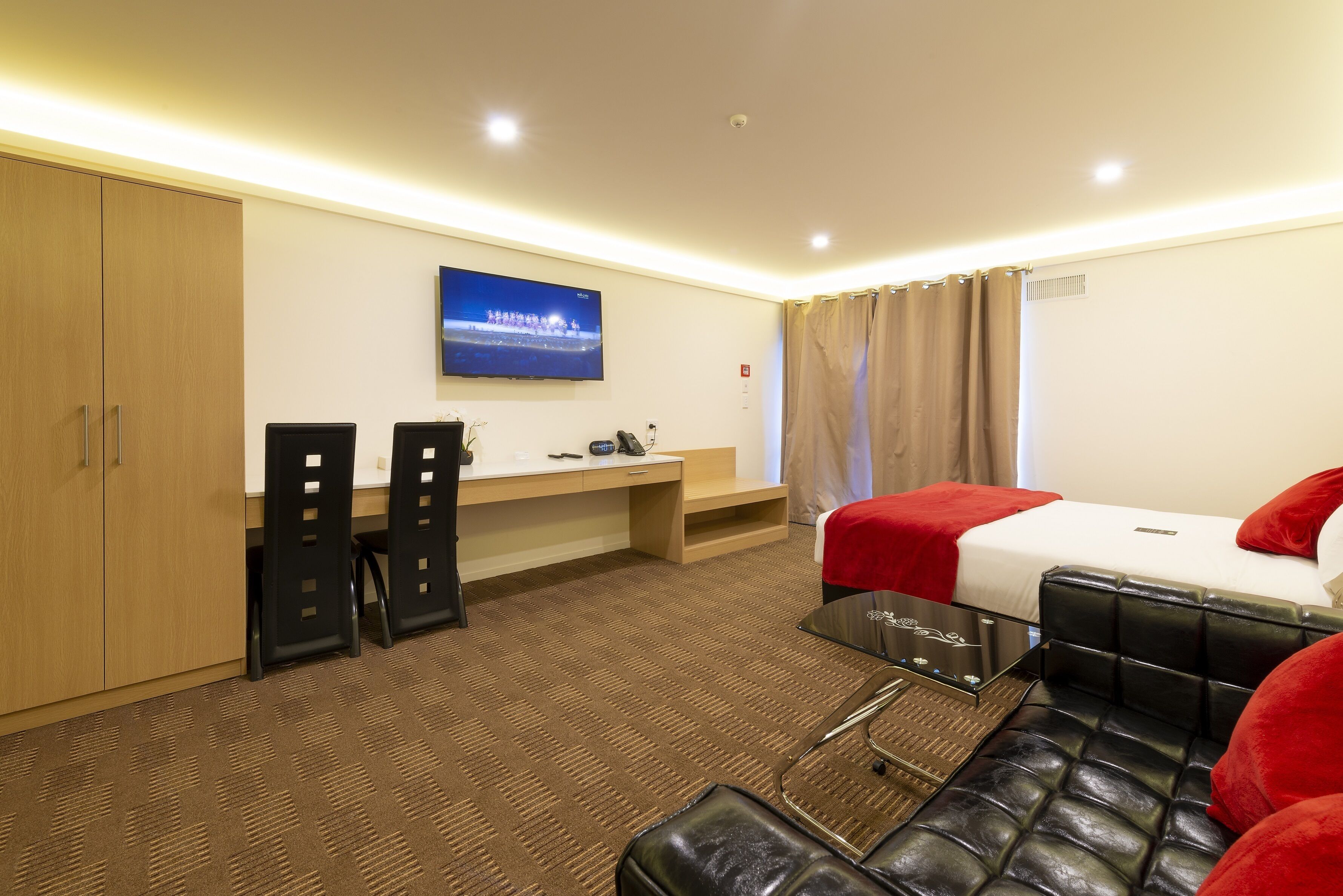 Habitación de hotel con cama, escritorio, silla, televisor y armario.