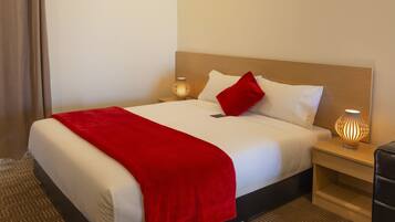 Een net opgemaakt bed met een rode plaid, witte kussens en een houten hoofdbord. Aan weerszijden van het bed staan twee nachtlampjes.