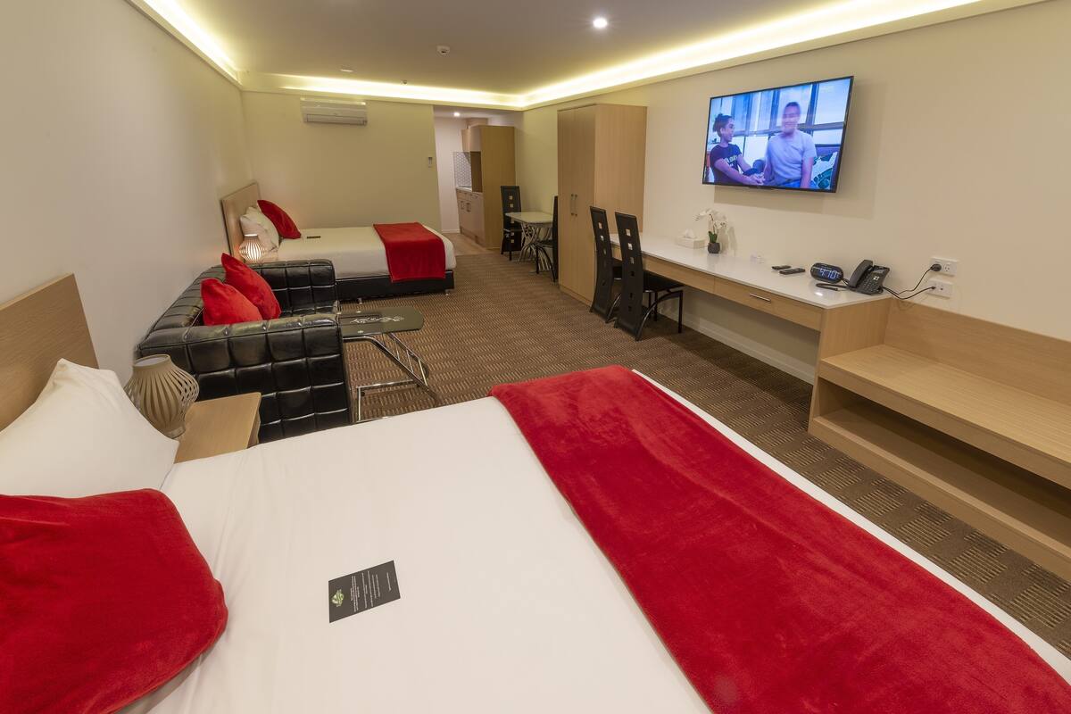 A hotel room with two beds, a desk, a TV, and a kitchenette.