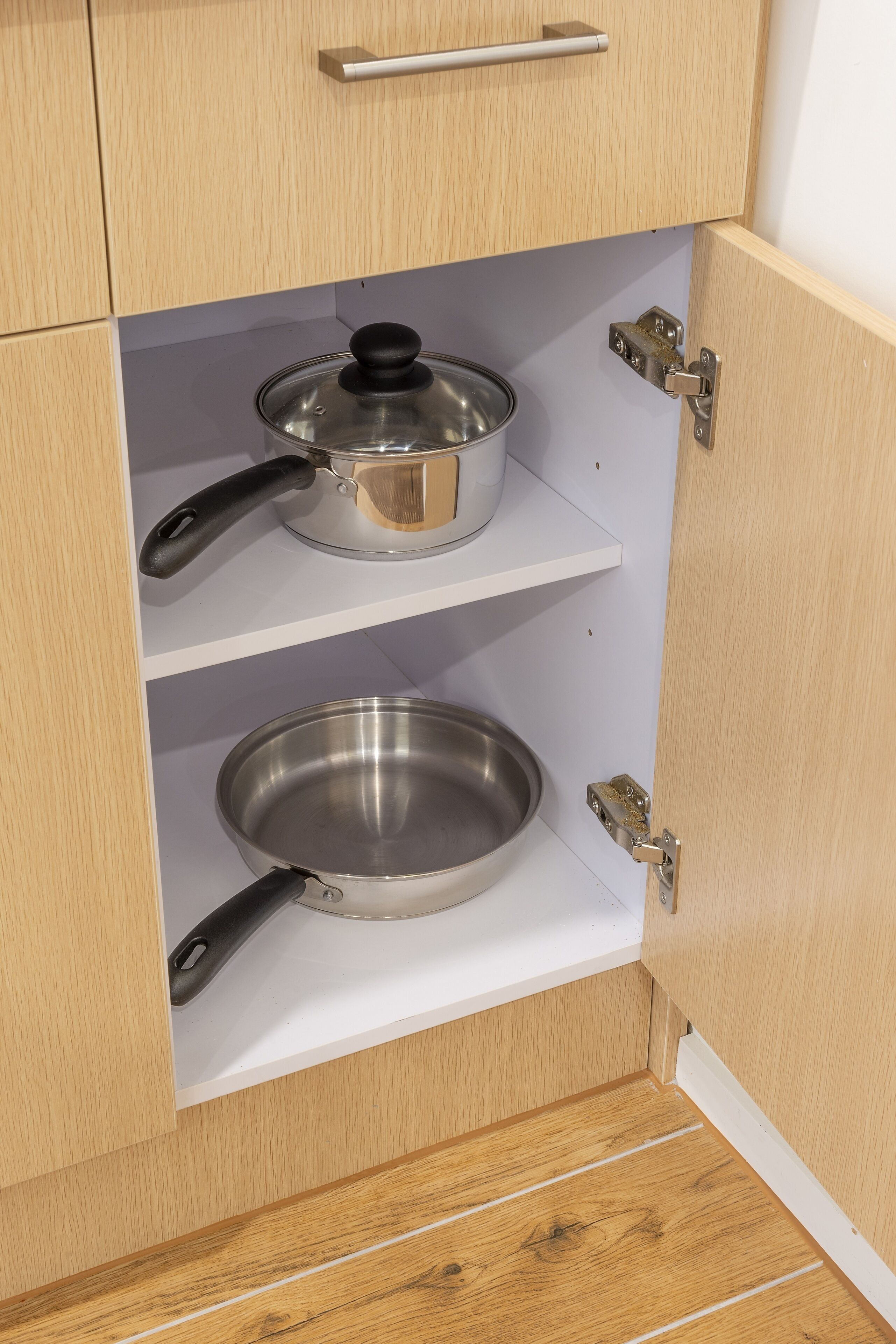 A kitchen cabinet with two stainless steel pots on shelves.