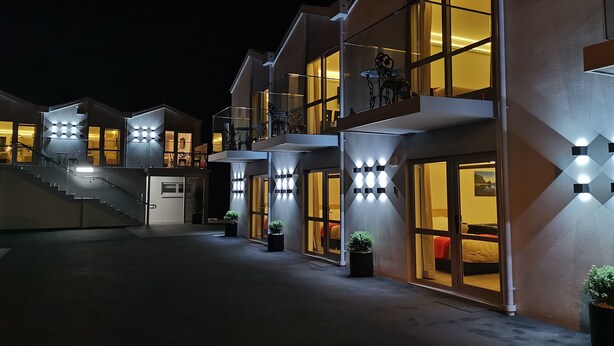 A modern hotel with multiple floors, outdoor seating, and illuminated entryways. - V Motel (Christchurch)