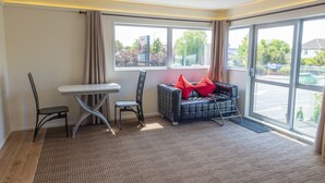 A modern room with a large window, a sofa with red cushions, a small table, and two chairs. - V Motel (Christchurch)