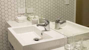 A modern bathroom with a white sink, two faucets, and a mirror. There are three glasses on the sink counter.