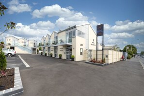 A modern motel with a glass facade, numbered 136, featuring a parking lot and a pedestrian pathway. - V Motel (Christchurch)