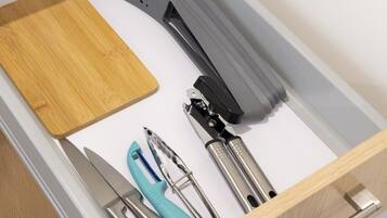 A drawer with a wooden cutting board, a grater, and various kitchen utensils.