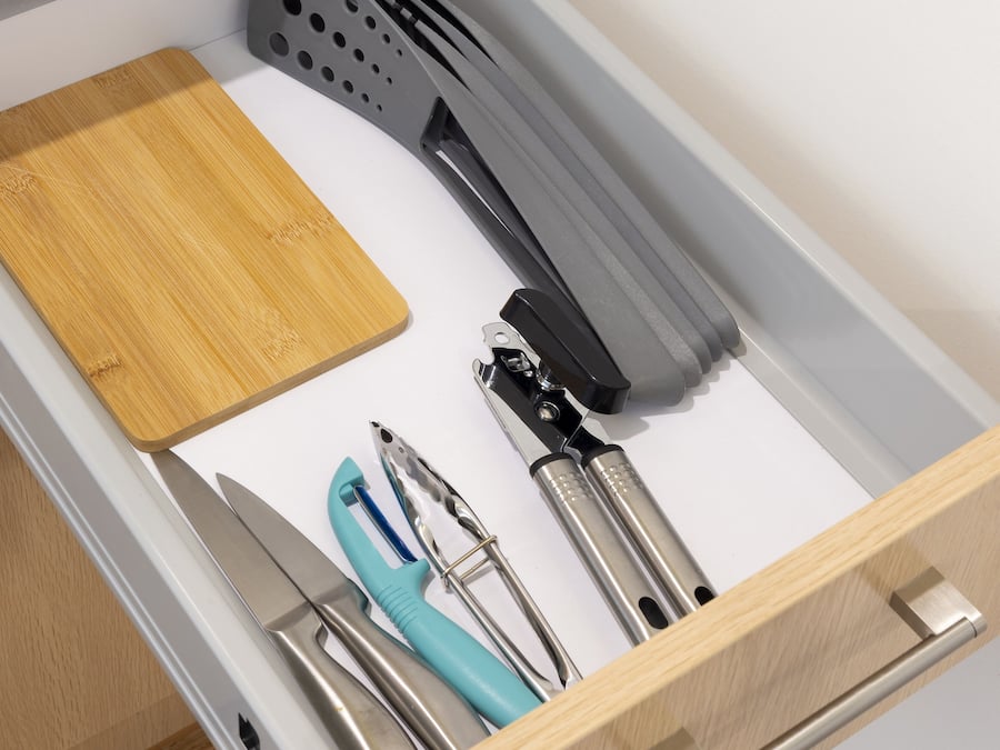 A drawer with a wooden cutting board, a grater, and various kitchen utensils.
