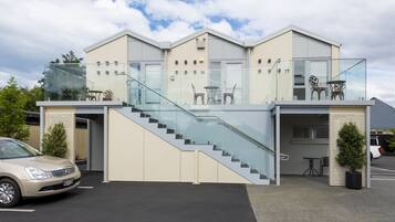 A modern building with a glass staircase, a car parked in front, and outdoor seating on the upper level.