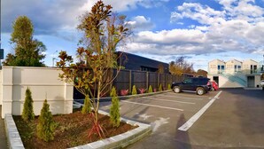 A parking lot with a black SUV, a building with a modern design, and a clear sky with clouds. - V Motel (Christchurch)