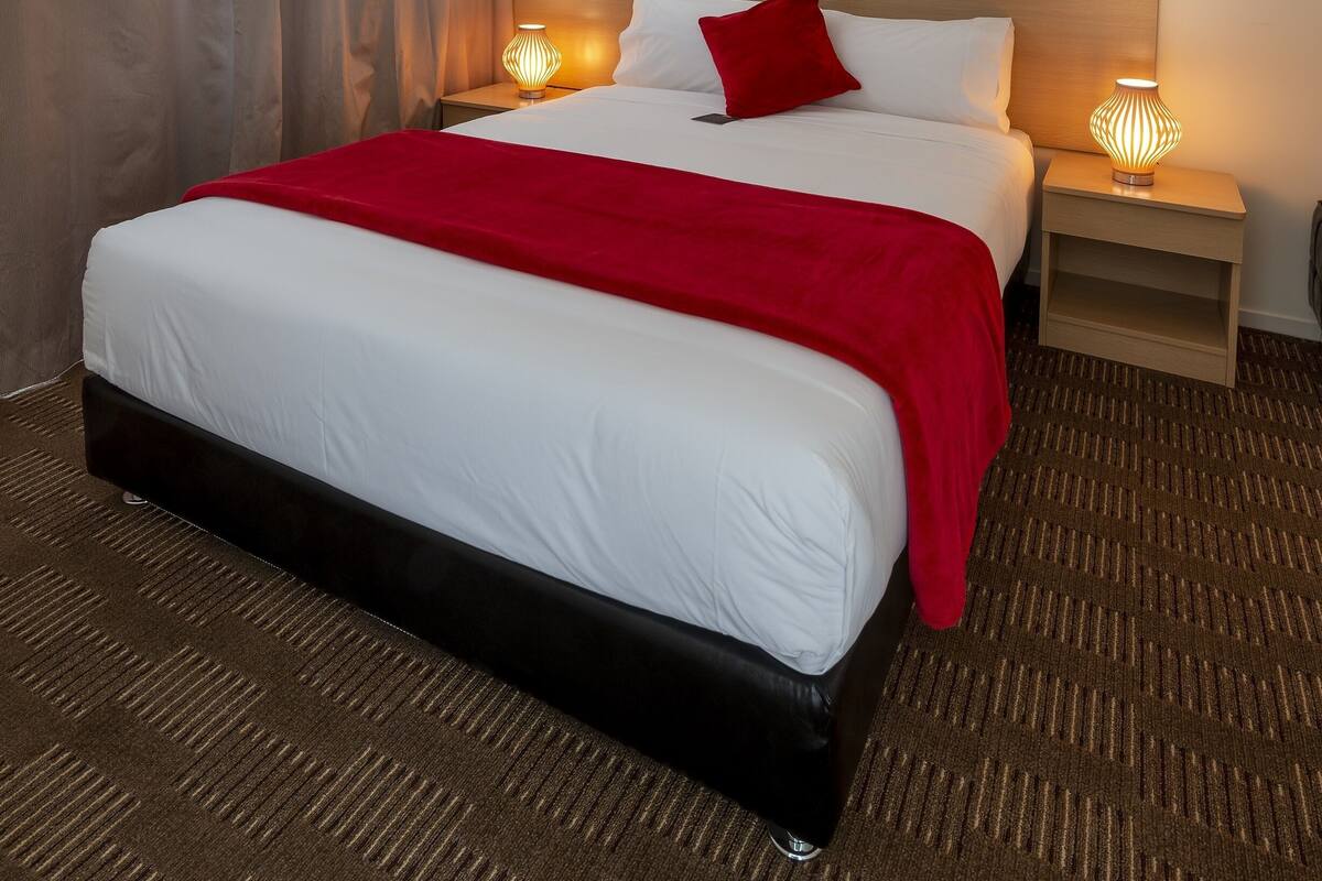 A hotel room with a large bed, a nightstand with a lamp, and a headboard.