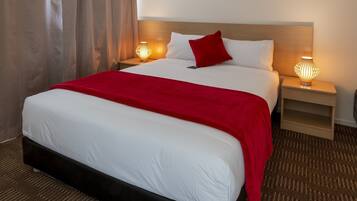 Quarto de hotel com uma cama grande, mesa de cabeceira com abajur e cabeceira.