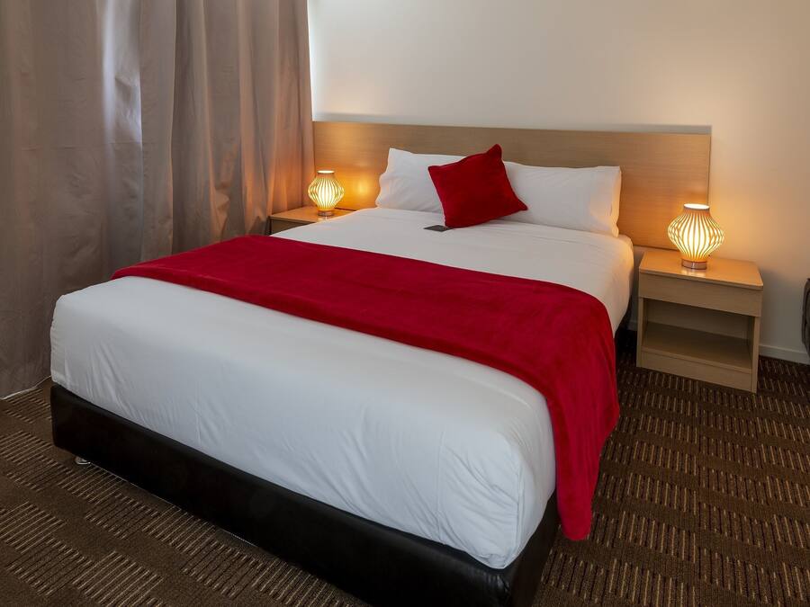 Quarto de hotel com uma cama grande, mesa de cabeceira com abajur e cabeceira.