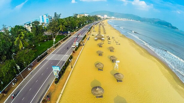 A beach with a road parallel to the shore, palm trees, and beach umbrellas. - Thiên Các 2 (Quy Nhon)