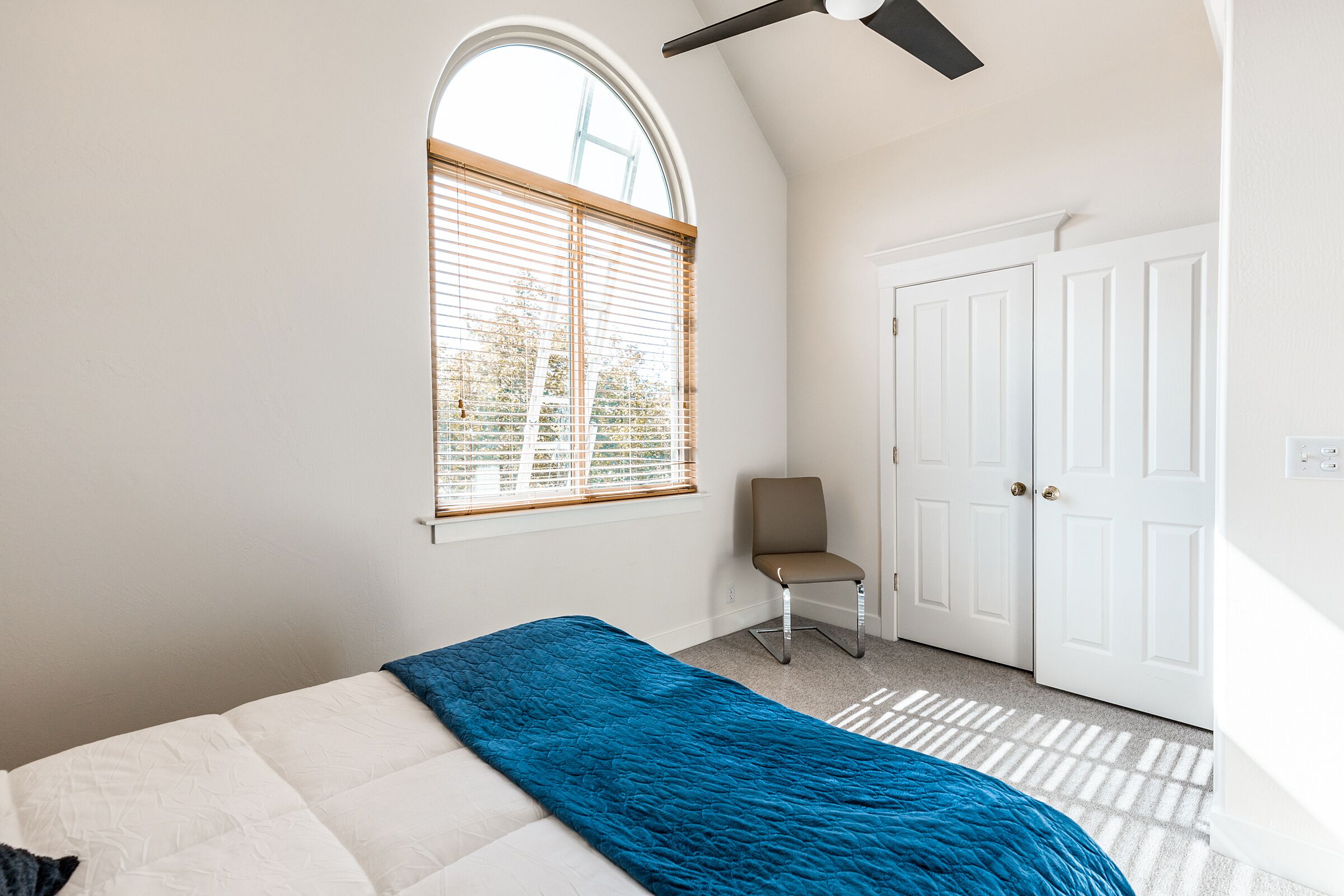 A bedroom with a bed, a window with blinds, a chair, and a door.