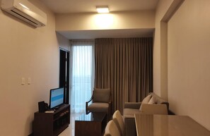 Une chambre d’hôtel moderne dotée d’une télévision à écran plat, d’un canapé, d’une table à manger et d’une grande fenêtre avec des rideaux.