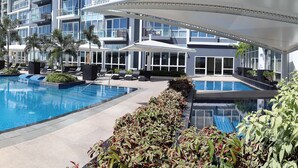 A modern hotel with a large rectangular pool, multiple lounge areas, and a view of high-rise buildings in the background. - 8 Newtown Boulevard by SIET (Lapu-Lapu)