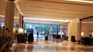 A spacious lobby with a polished floor, seating areas, and large windows offering a view of greenery outside. - 8 Newtown Boulevard by SIET (Lapu-Lapu)