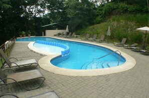 Ein Schwimmbecken mit gebogener Form, umgeben von Liegestühlen und Sonnenschirmen.
