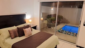 Une chambre à coucher avec un lit, des lampes de chevet et une porte-fenêtre coulissante donnant sur un balcon avec une piscine.