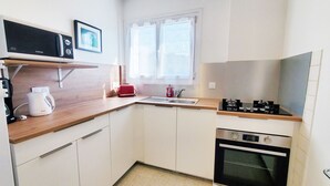 Et kompakt køkken med hvide skabe, en mikrobølgeovn, en brødrister, en elkedel og en lille ovn.